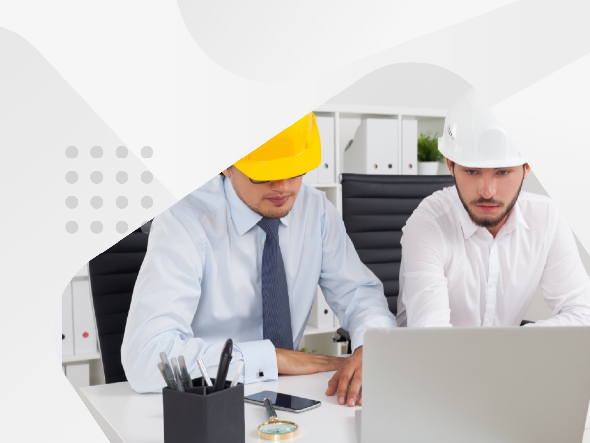 Two men in hard hats collaborating on a laptop, engaged in a construction project.