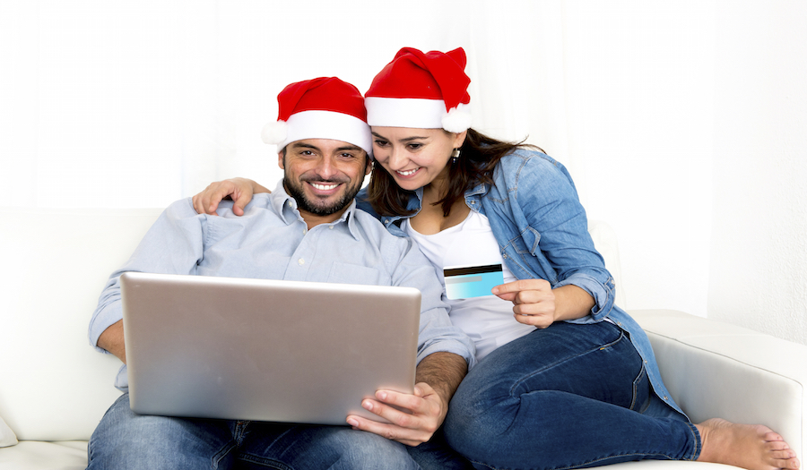 young attractive Hispanic couple in love sitting together on sofa couch at home living room with computer laptop shopping online Christmas presents with credit card on internet