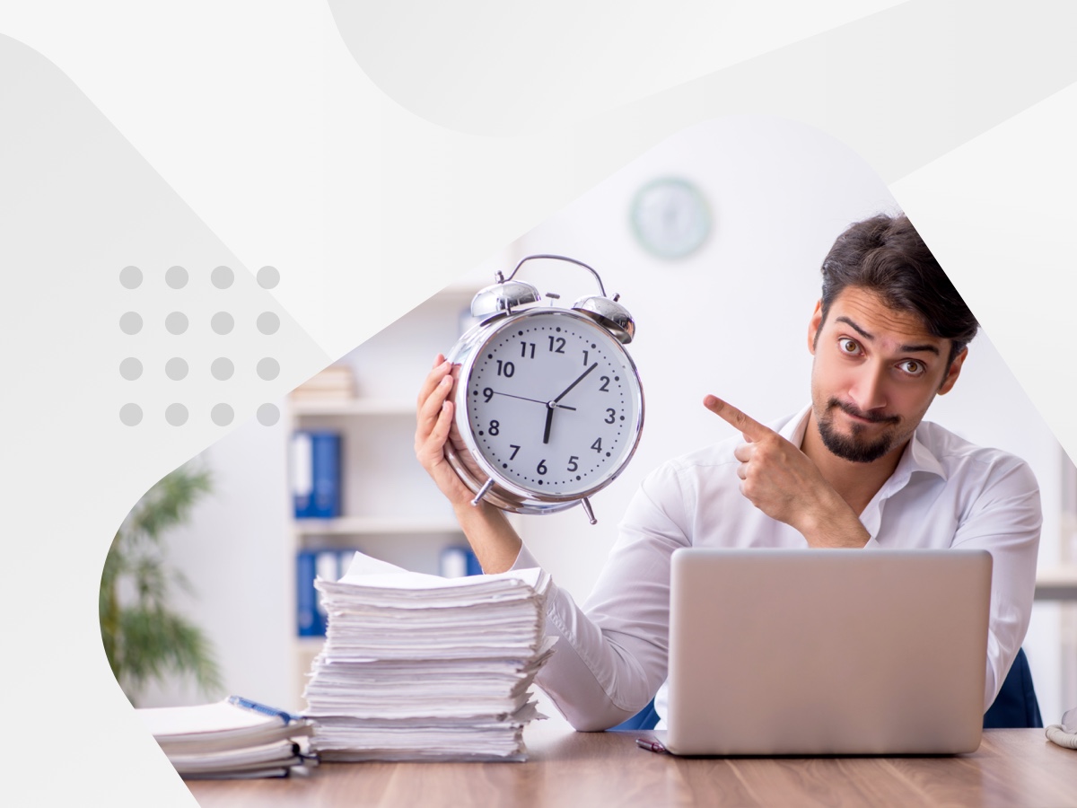 A person with a clock and laptop at a work desk.