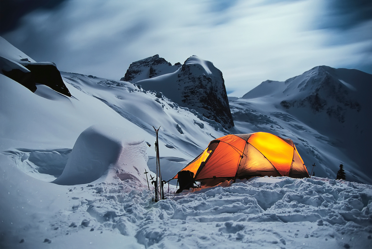 Tent in winter on a mountain top at night in the Carpathians. Bright yellow tourist tent in the snowy mountains nature